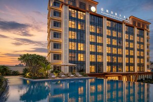 A hotel with a swimming pool and a view of the city skyline at dusk.