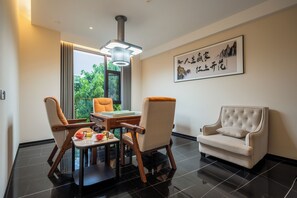 Ein modernes Wohnzimmer mit Esstisch, zwei Stühlen, einer Couch und einem großen Fenster mit Blick auf Grünflächen.