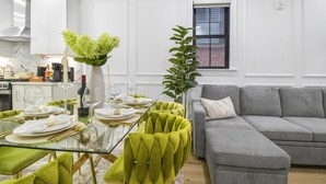A modern kitchen with white cabinetry, a dining table set for six, and a grey sofa in the living area. - North End Apartment Prime Location (Boston)