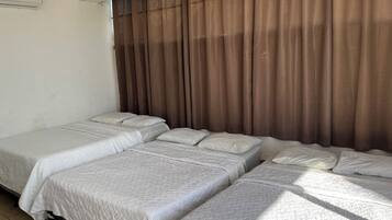 A hotel room with two single beds, a large window with brown curtains, and an air conditioning unit on the wall.