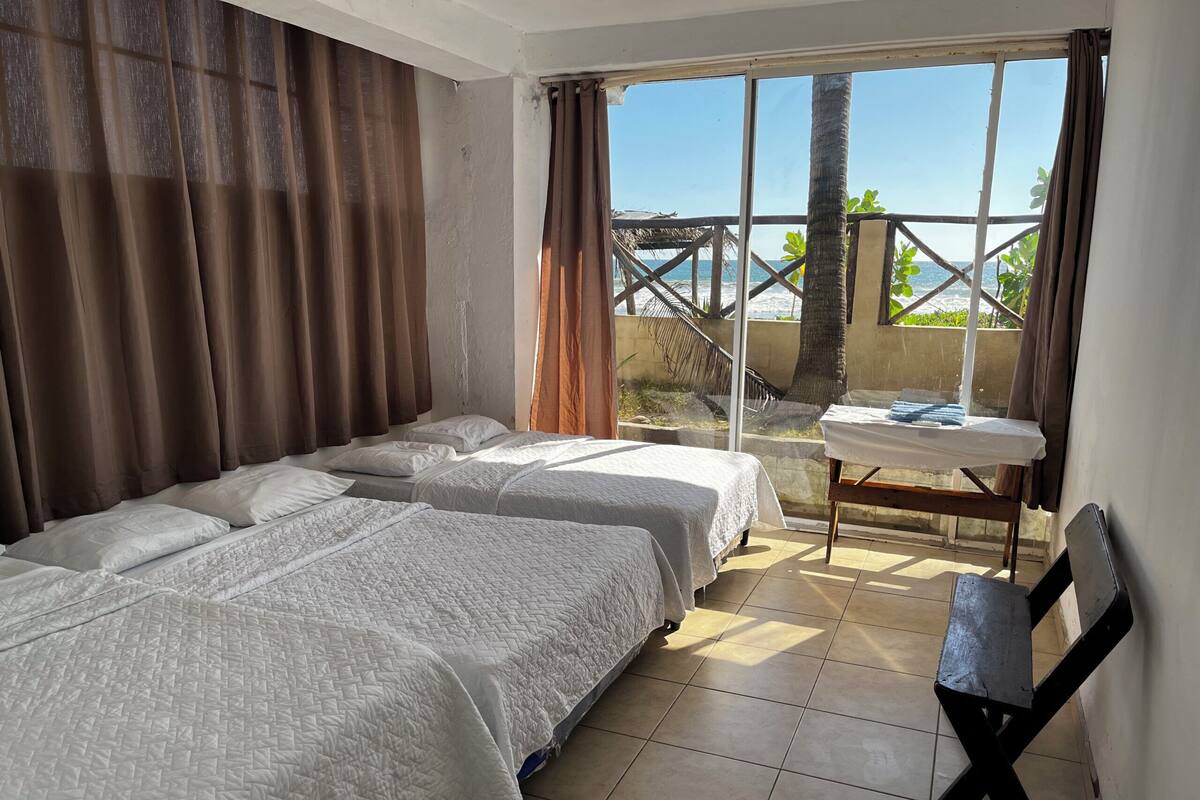 Una habitación con dos camas, una mesa y vista al mar.