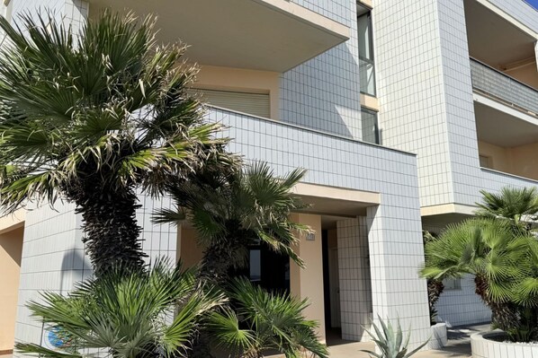 Un edificio moderno con fachada de tejas, balcones y palmeras circundantes.