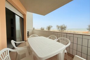 Un balcón con mesa y sillas blancas, un muro con azulejos y vista a la playa.