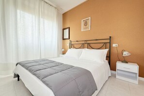 Un dormitorio con cama, mesita de noche, lámpara, un cuadro en la pared y una ventana con cortinas.