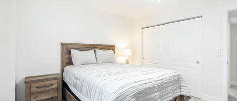 Quarto com cama, mesa de cabeceira, abajur e porta.