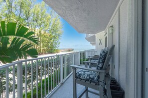 Ein Balkon mit Blick auf das Meer, einem weißen Geländer und einem Sessel mit floralem Kissen.