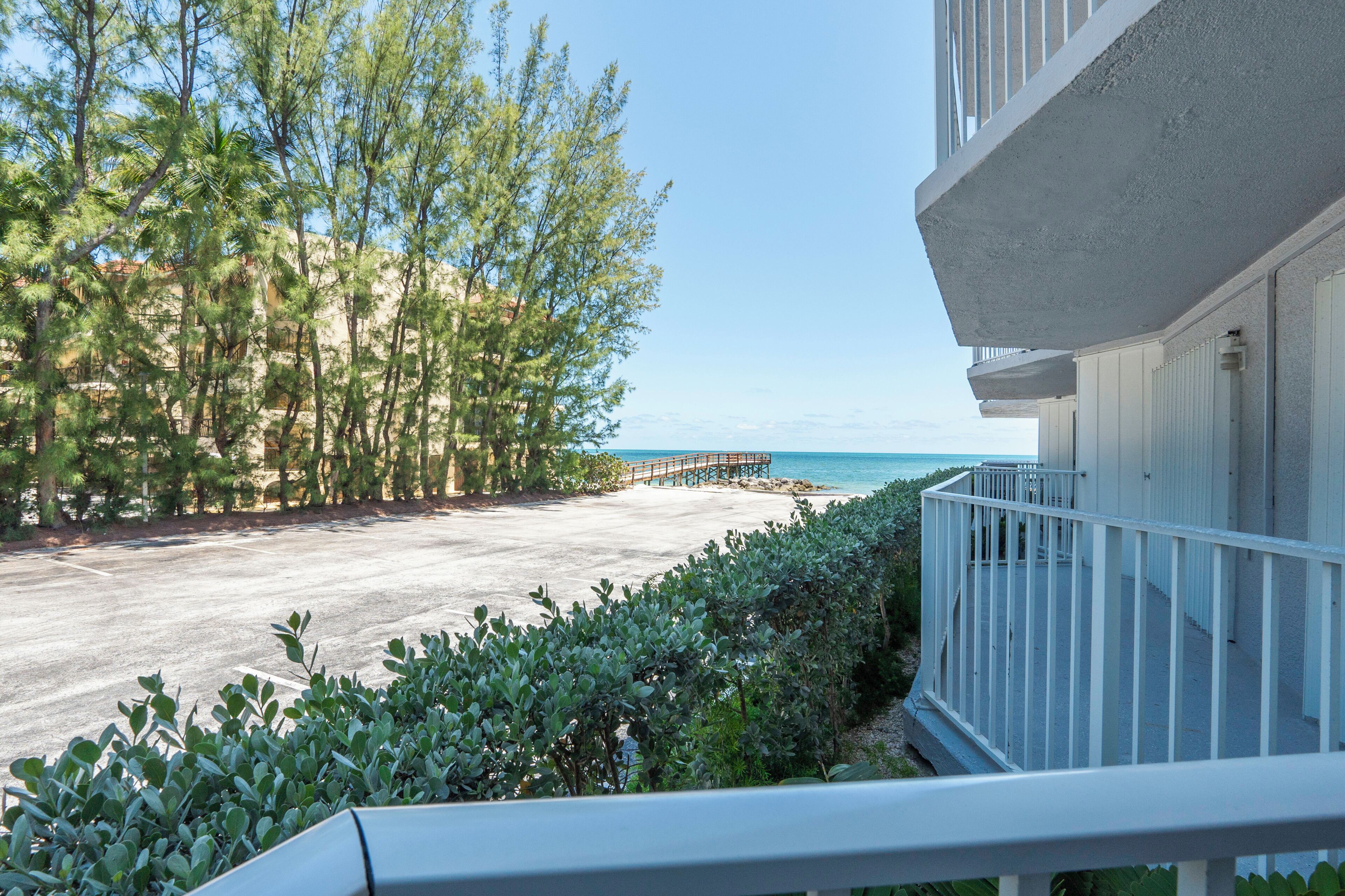 A beachfront view with a wooden pier, a building with a balcony, and dense greenery.