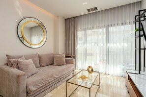 Una sala de estar moderna con un sofá, un espejo redondo, una mesa de centro de vidrio y cortinas translúcidas.