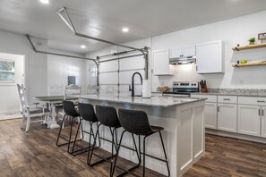 A modern kitchen with white cabinets, a central island with bar stools, a stainless steel range hood, and a built-in oven. - 3-bedroom LakeFRONT house with seperate gameroom! (Garfield)