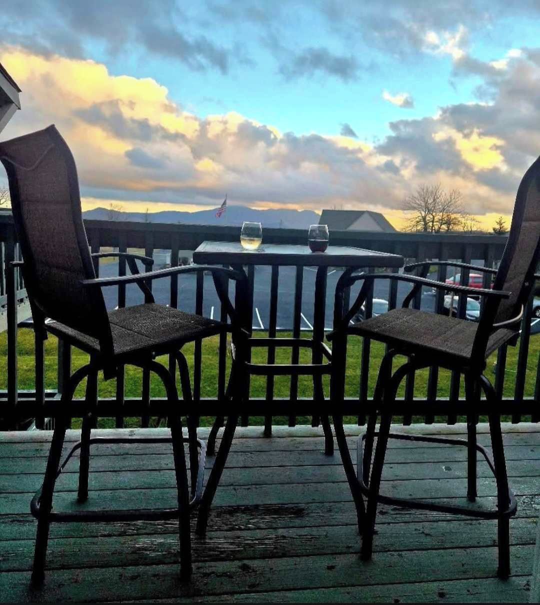 A deck with two chairs and a table, overlooking a body of water and distant mountains.