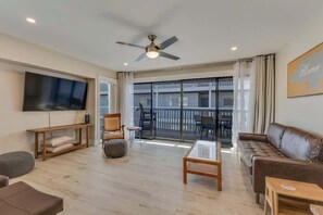 Un salon moderne doté d’un téléviseur à écran plat, d’un ventilateur de plafond, d’un canapé, d’une table basse et d’un balcon avec des sièges d’ext érieur.