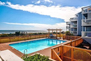 Une piscine avec une terrasse en bois, un espace salon couvert et une vue sur la plage.