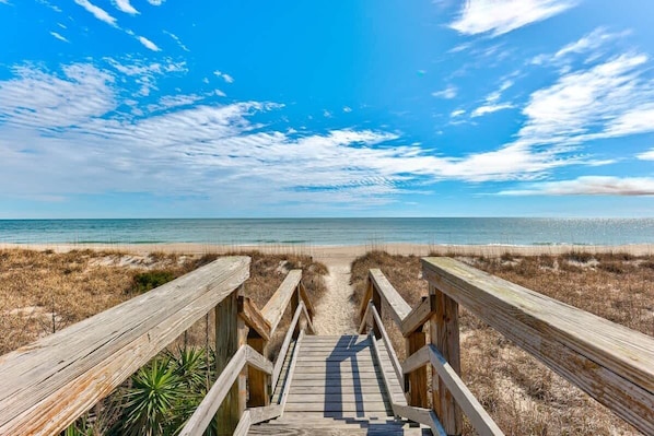 Une promenade en bois menant à une plage, avec un ciel dégagé.