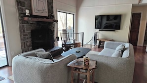 A living room with a stone fireplace, a television mounted on the wall, and a large window. - Private homes Beech Mountain! (Beech Mountain)