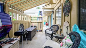 A covered outdoor seating area with wicker furniture, a table, and a surfboard decoration. - Renovated 2BR First Floor Forest Beach Condo (Hilton Head Island)