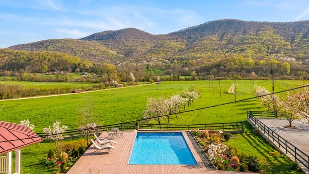 A swimming pool with a deck, surrounded by a garden with flowers and trees, set against a backdrop of green fields and mountains. - Gorgeous home in Buzim (Buzim)