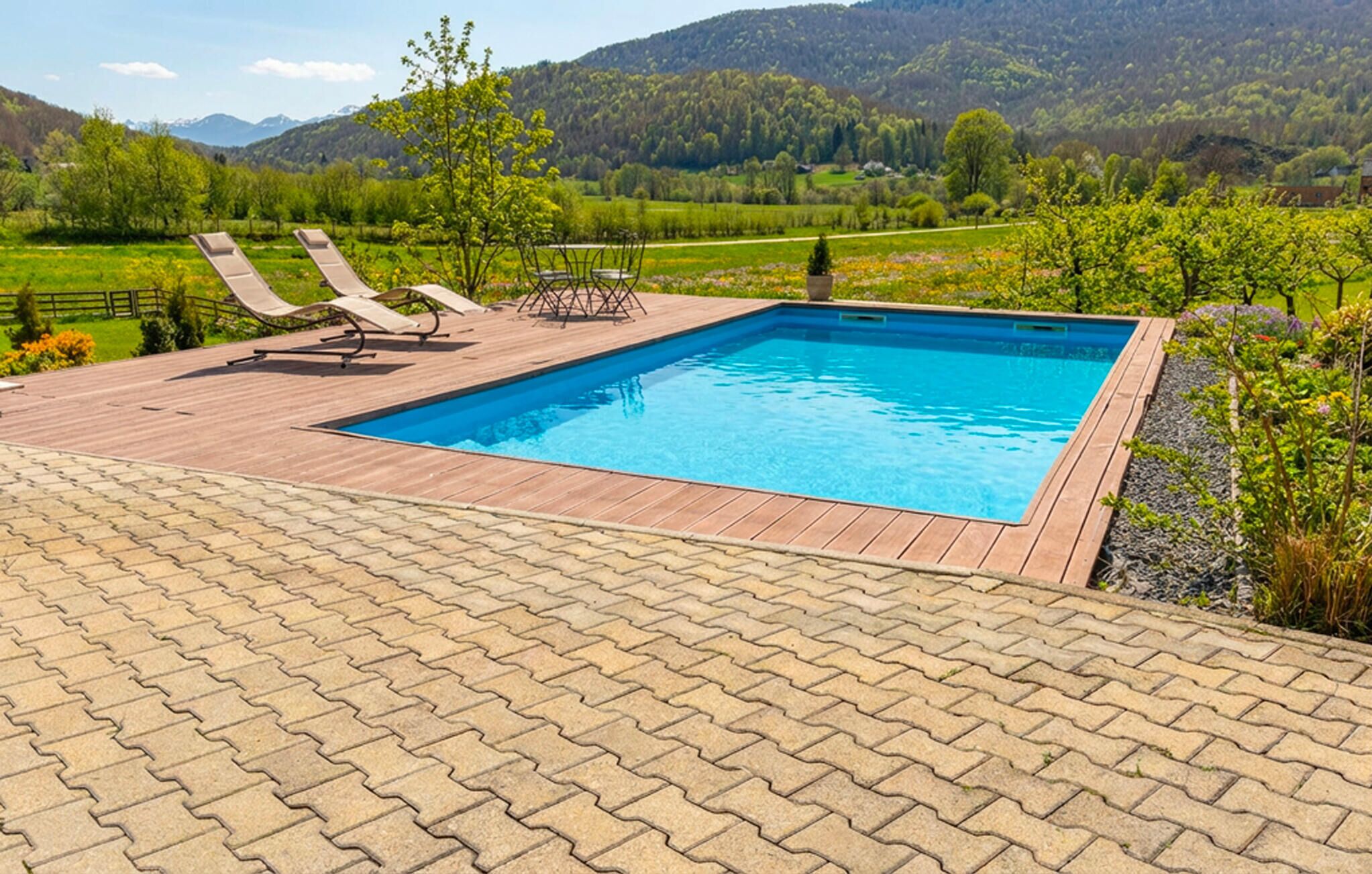 A rectangular swimming pool with a wooden deck, two lounge chairs, and a table.