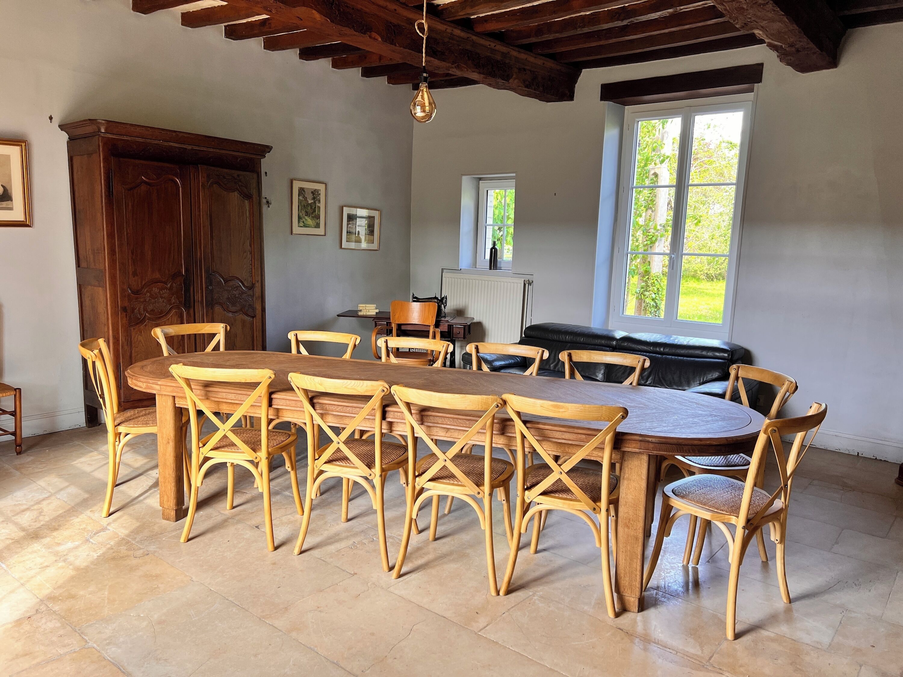 A dining area with a wooden table and chairs, a large wooden cabinet, and a window with a view of greenery.