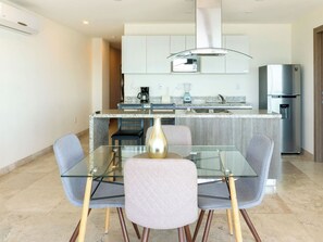 Een moderne keuken met een glazen eettafel, stoelen, een roestvrijstalen koelkast en een koffiezetapparaat.