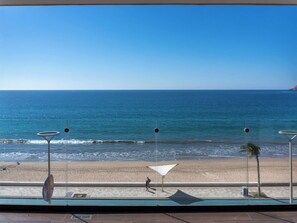 A beach view from a balcony with a clear sky, a sandy beach, and a calm sea. - Oceanfront apartment on the Malecon (Mazatlan)