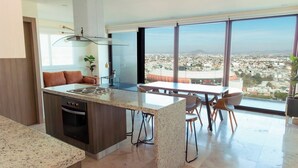 Een moderne keuken met een groot eiland, een eetgedeelte met stoelen en een panoramisch uitzicht over de stad.