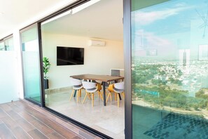 A modern interior with a dining area, a flat-screen TV, and a city view through large glass doors. - Elegante Apartamento en el Malecon Alberca Infinit (Mazatlan)