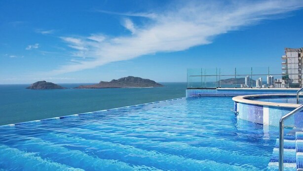 Een zwembad met helderblauw water, een glazen balustrade en uitzicht op zee en verre eilanden.