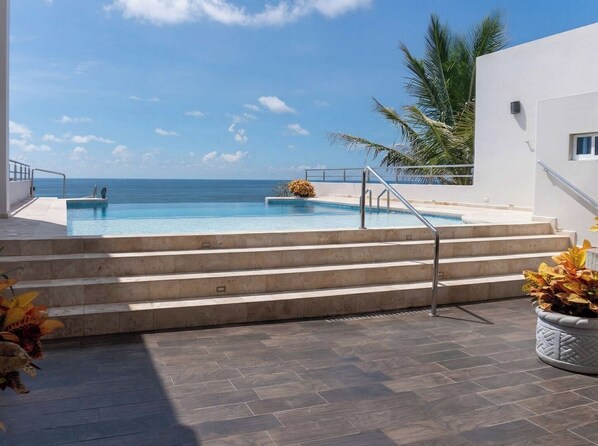 Una piscina con gradini che vi conducono, una palma e vista sull'oceano.