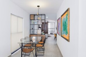 Uma sala de jantar moderna com mesa de vidro, cadeiras de metal e um lustre decorativo.