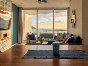 Un soggiorno moderno con una grande finestra vista mare, un divano, un tavolino da caffè e una TV.
