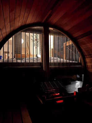 A dimly lit room with a curved wooden ceiling, a bed with a metal frame, and a window with vertical bars.
