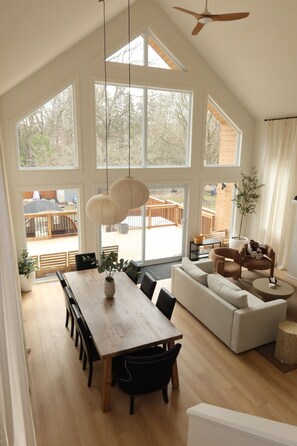 A spacious living area with a large dining table, sofas, and a ceiling fan.