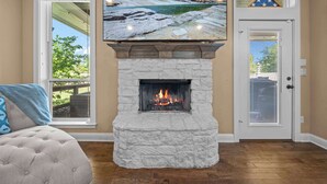 A fireplace with a stone surround, a television mounted above it, and a door with a window. - The Oasis at Stonebriar (Lindale)