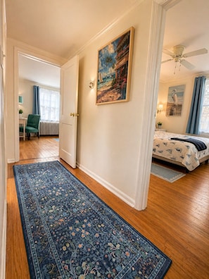 A hallway with a patterned rug, a painting, a bed with a patterned bedspread, and a ceiling fan. - NEW Coastal Cottage 2 Miles to Beach + Lake Access (Clinton)