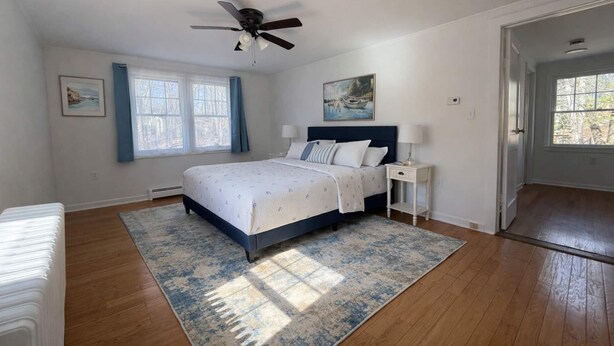 A bedroom with a bed, a ceiling fan, a nightstand, a window with curtains, and a door.