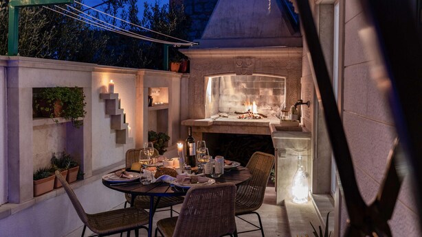 Un área de comedor al aire libre con chimenea de piedra, sillas de mimbre y una mesa preparada para una comida.