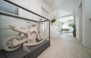 Ein Flur mit einer Motorradausstellung, ein Essbereich mit Stühlen und einem Tisch sowie eine Zimmerpflanze.