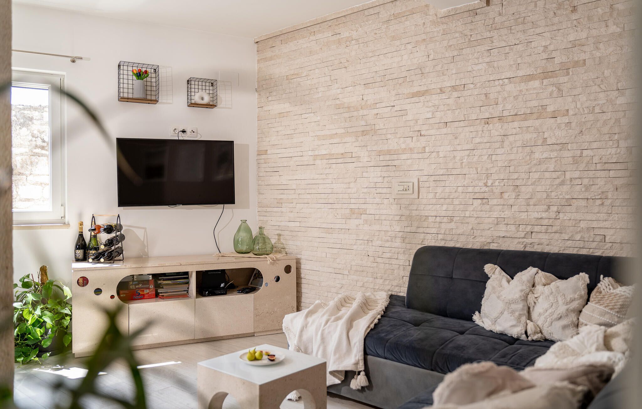 Ein Wohnzimmer mit Ziegelwand, Flachbildfernseher, dunklem Sofa und einem kleinen Tisch mit Pflanze.