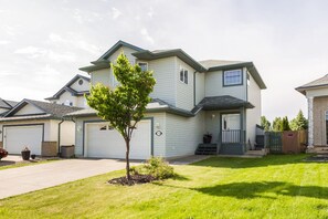 A two-story house with a front garage, a small front yard with a tree, and a clear sky. - Cozy 2BR Suite In Lewis Estates Golf Course By Henday/Whitemud-Long Stay Suite! (Edmonton)