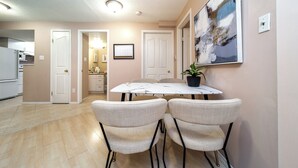 A dining area with a marble table, four upholstered chairs, a potted plant, and a painting on the wall. - Cozy 2BR Suite In Lewis Estates Golf Course By Henday/Whitemud-Long Stay Suite! (Edmonton)