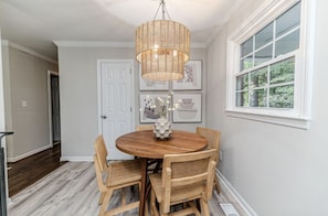 A dining area with a round wooden table, four wicker chairs, a woven pendant light, and framed artwork on the wall. - Cute! 3BR house near DT Raleigh (Garner)