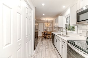 A kitchen with white cabinets, a wooden dining table, and a modern microwave. - Cute! 3BR house near DT Raleigh (Garner)