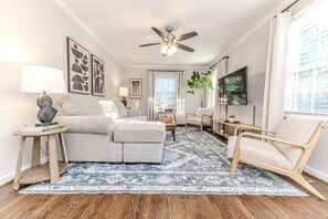 A living room with a ceiling fan, a sofa, a chair, a coffee table, and a TV. - Cute! 3BR house near DT Raleigh (Garner)
