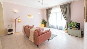 A living room with a sofa, a television, a floor lamp, and a ceiling fan. - Cozy 1-bedroom resort in beautiful L-Għarb with AC and gym (L-Għarb)