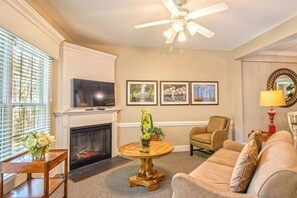 A living room with a fireplace, a ceiling fan, a television, and a sofa.