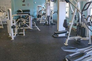 A gym with various exercise machines, a Cybex brand treadmill, and a wall-mounted TV.