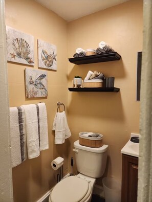 A bathroom with a toilet, a sink, a towel rack with towels, and artwork on the wall. - Newark Furnished Apartment for World Cup (Newark)