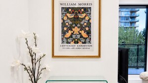 Ein gerahmtes Kunstwerk mit dem Titel 'William Morris' in einem modernen Interieur mit einem Glastisch und einer weißen Vase mit Blumen.