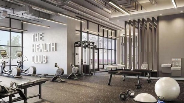 Ein modernes Fitnessstudio mit Trainingsgeräten, einer Wand mit der Aufschrift 'THE HEALTH CLUB' und großen Fenstern.
