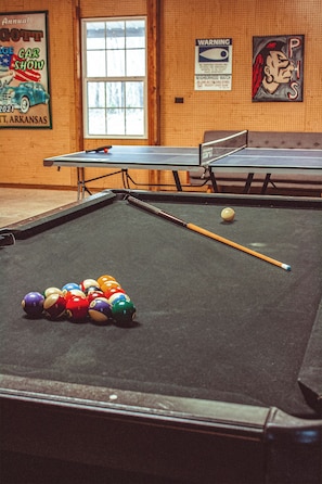 A pool table with balls, a cue stick, and a poster on the wall.